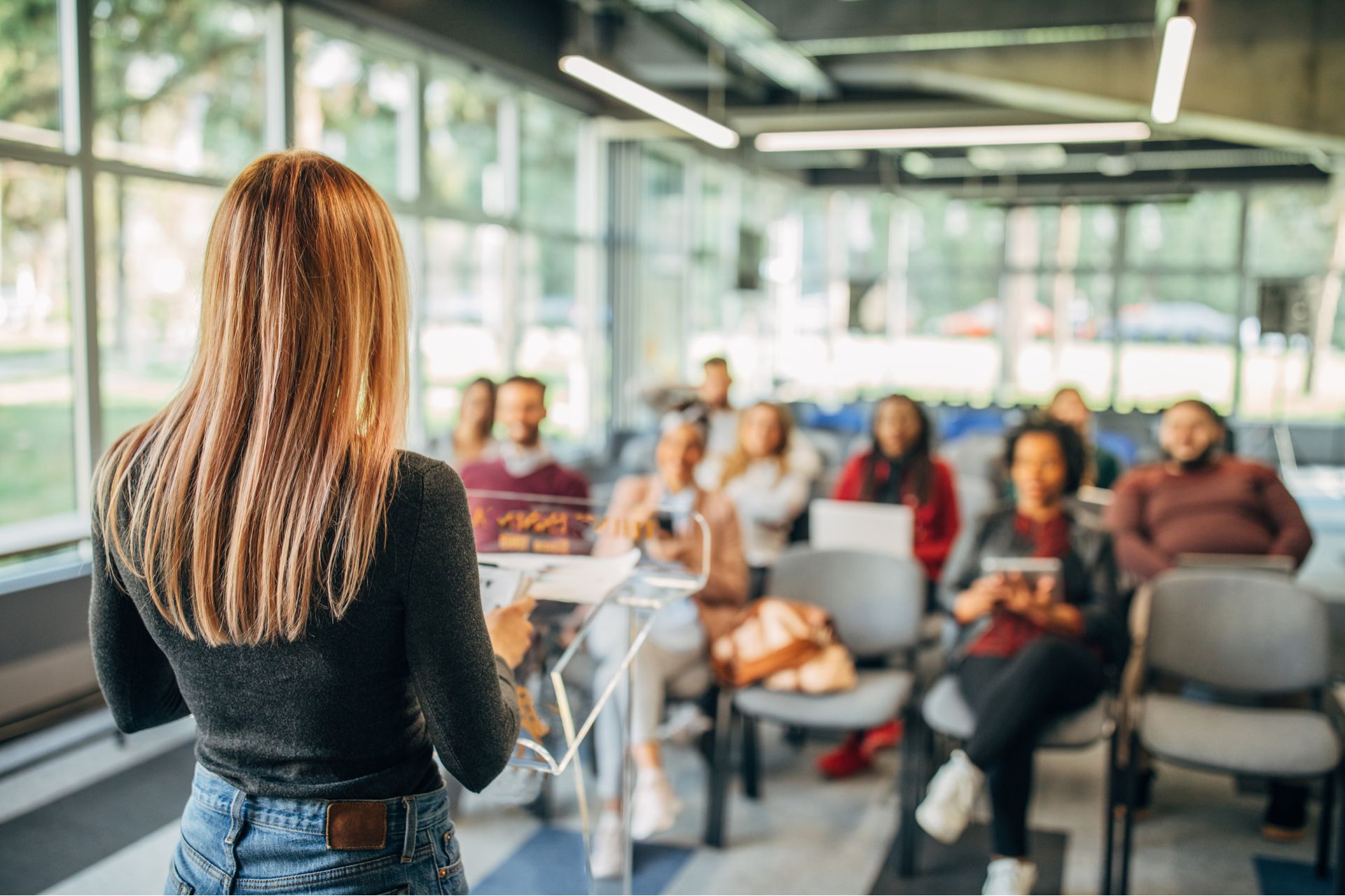 A group of people in a conference room A person standing and talking to a room full of people