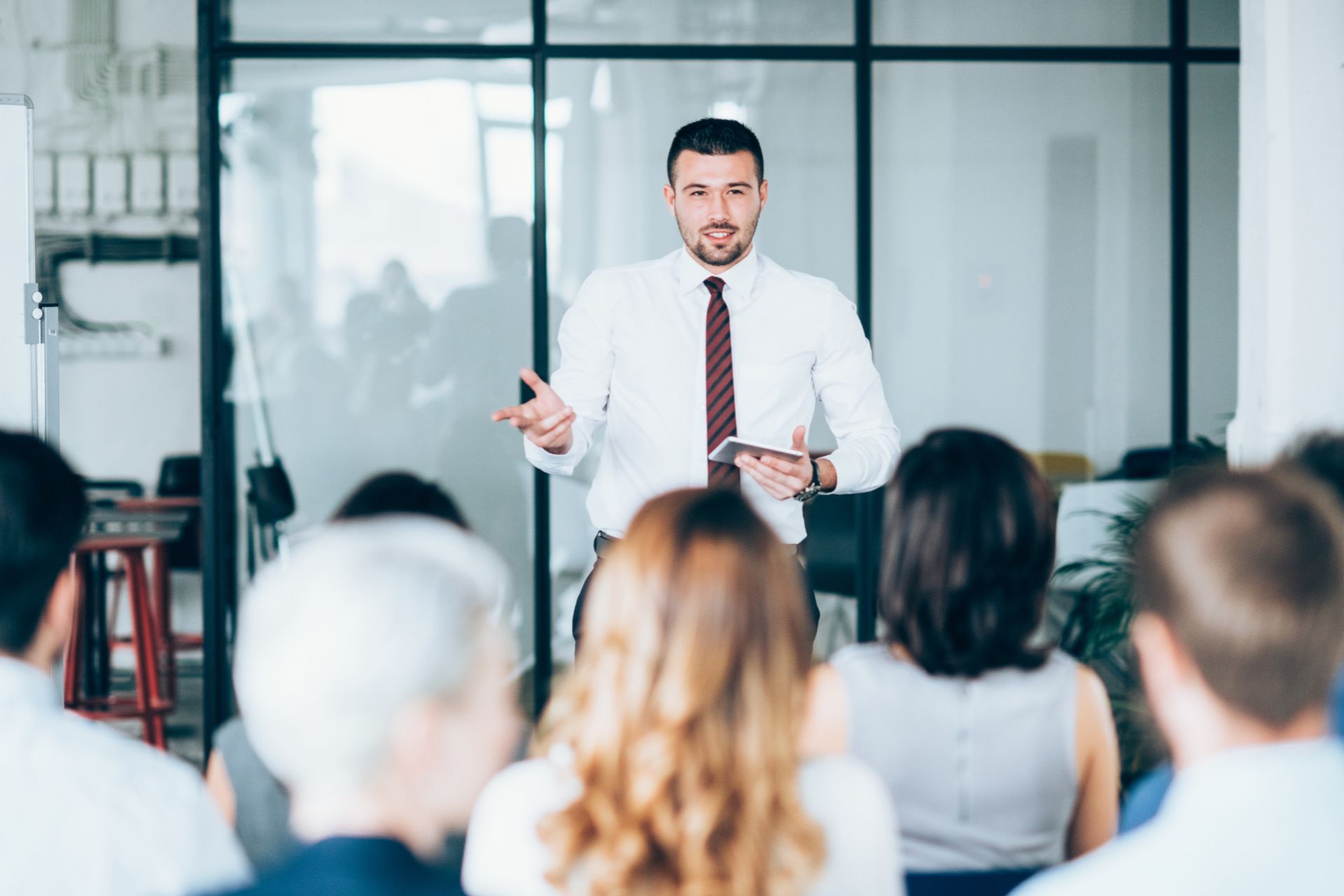 A man talking to a group of individuals with a glass wall behind him. This is to represent a training meeting.